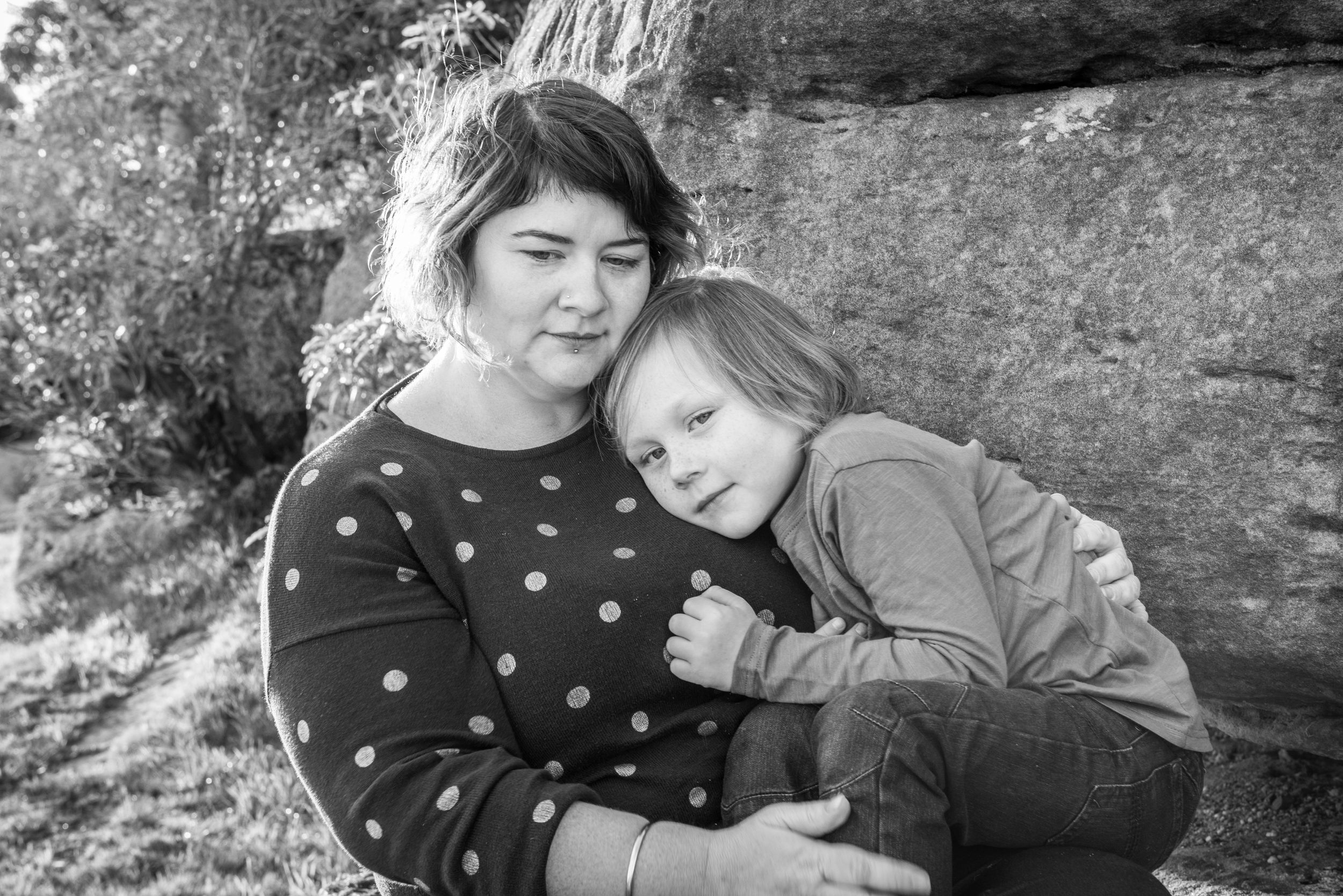 Black and white portrait of two people cuddling against rocky backdrop.