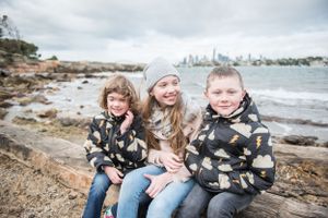 Coastal family lifestyle photography with rocky shoreline and city skyline views in background.
