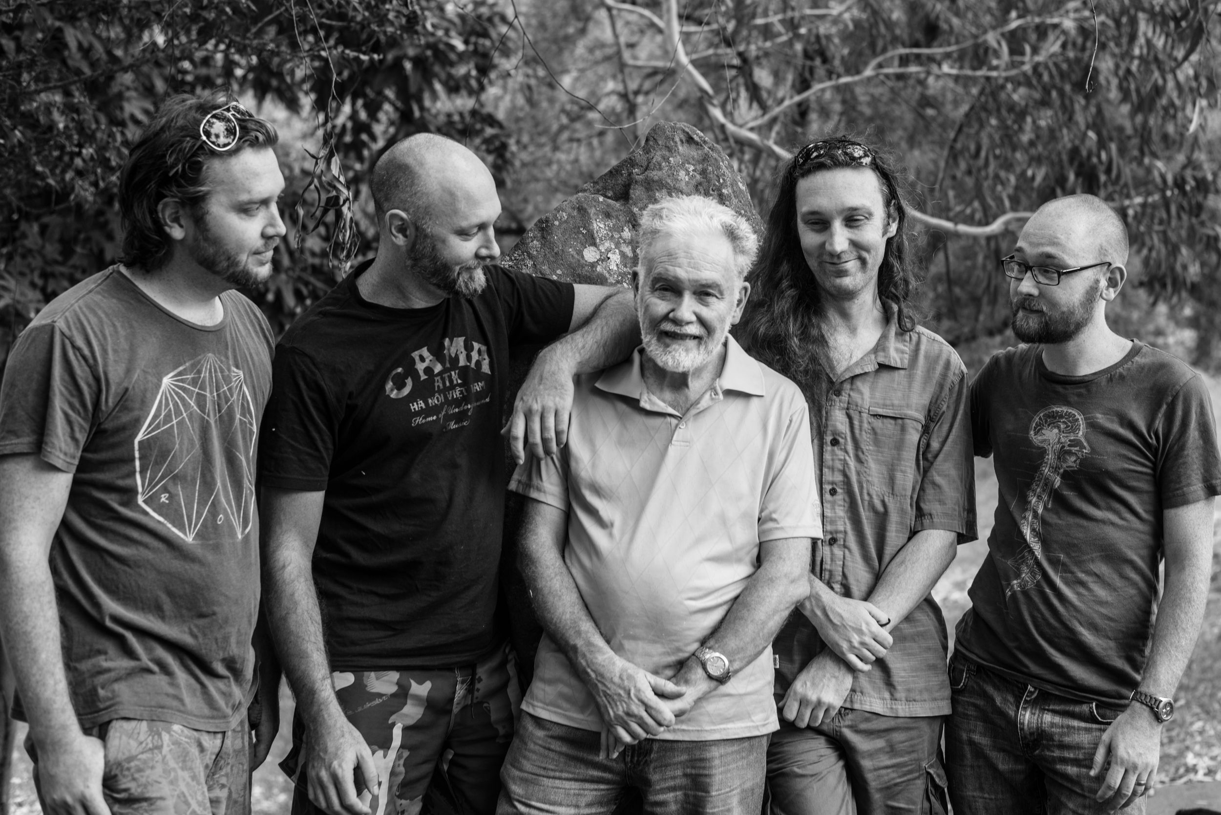 Black and white group photo of five musicians standing together outdoors.