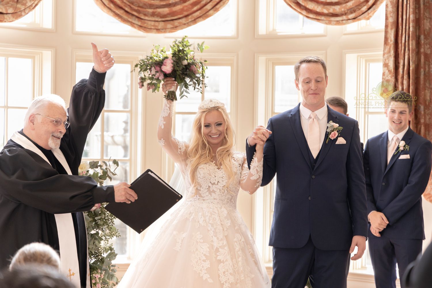 A celebratory moment during a wedding ceremony in an elegant room with draped windows.