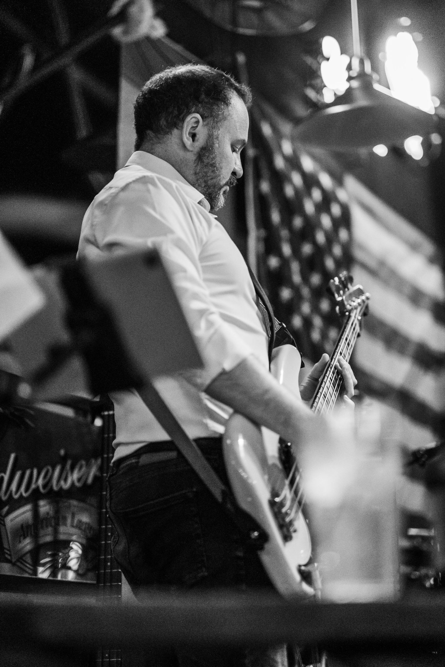 Black and white image of a man playing a bass guitar in front of an American flag.