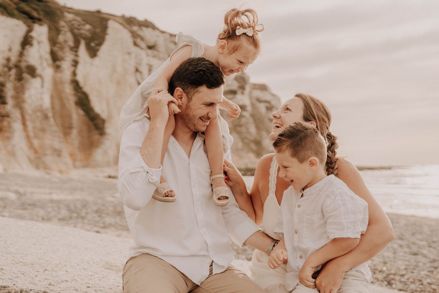 Family enjoying a playful moment together on a sandy beach near scenic cliffs on a warm day.