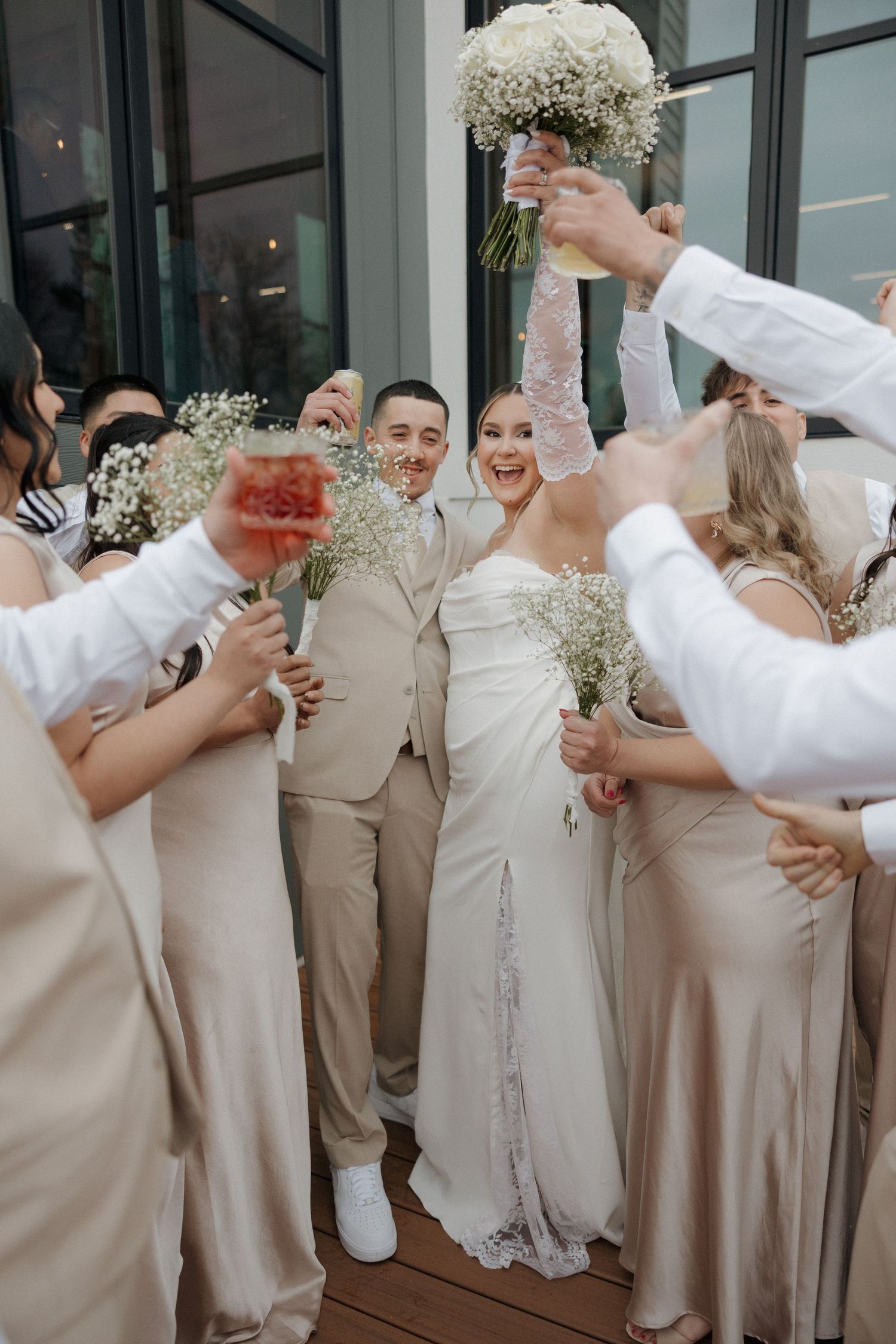 Wedding party wearing champagne-colored attire celebrates with raised drinks on outdoor patio.