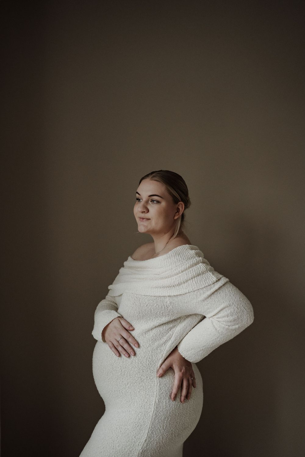 Artistic maternity portrait featuring figure in white textured sweater dress against neutral backdrop.