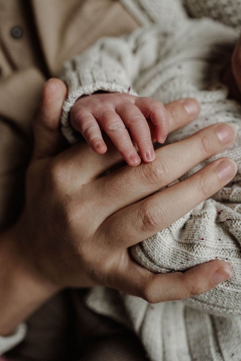 A tiny baby's hand gently rests on an adult's palm, wrapped in soft knitted fabric.