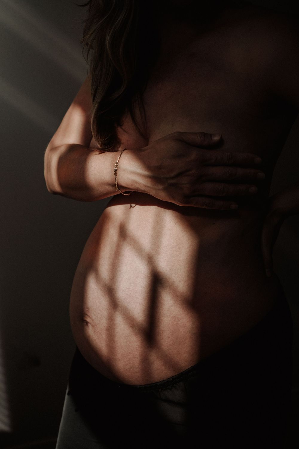Artistic silhouette of a pregnant belly with hands creating shadows in dramatic lighting.