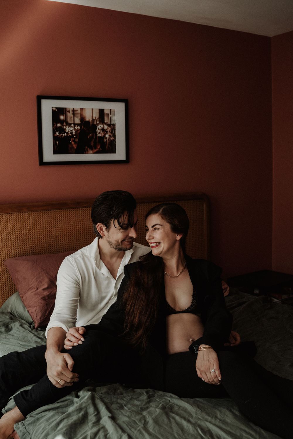 A couple laughing together on a bed with burgundy walls and vintage decor.