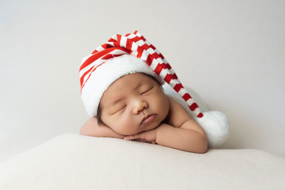 Sleeping newborn wearing red and white striped holiday hat on white background.