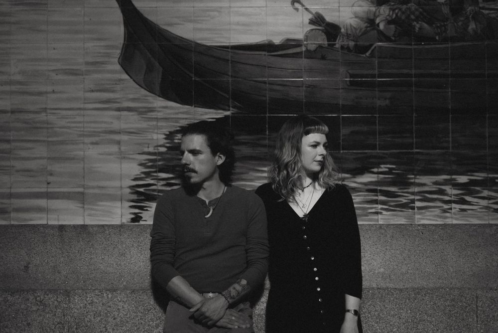 Black and white portrait of a couple standing against a maritime wall mural.