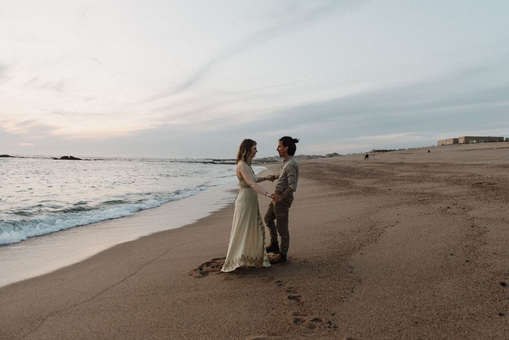 A romantic couple in formal attire embracing on a serene beach at sunset.
