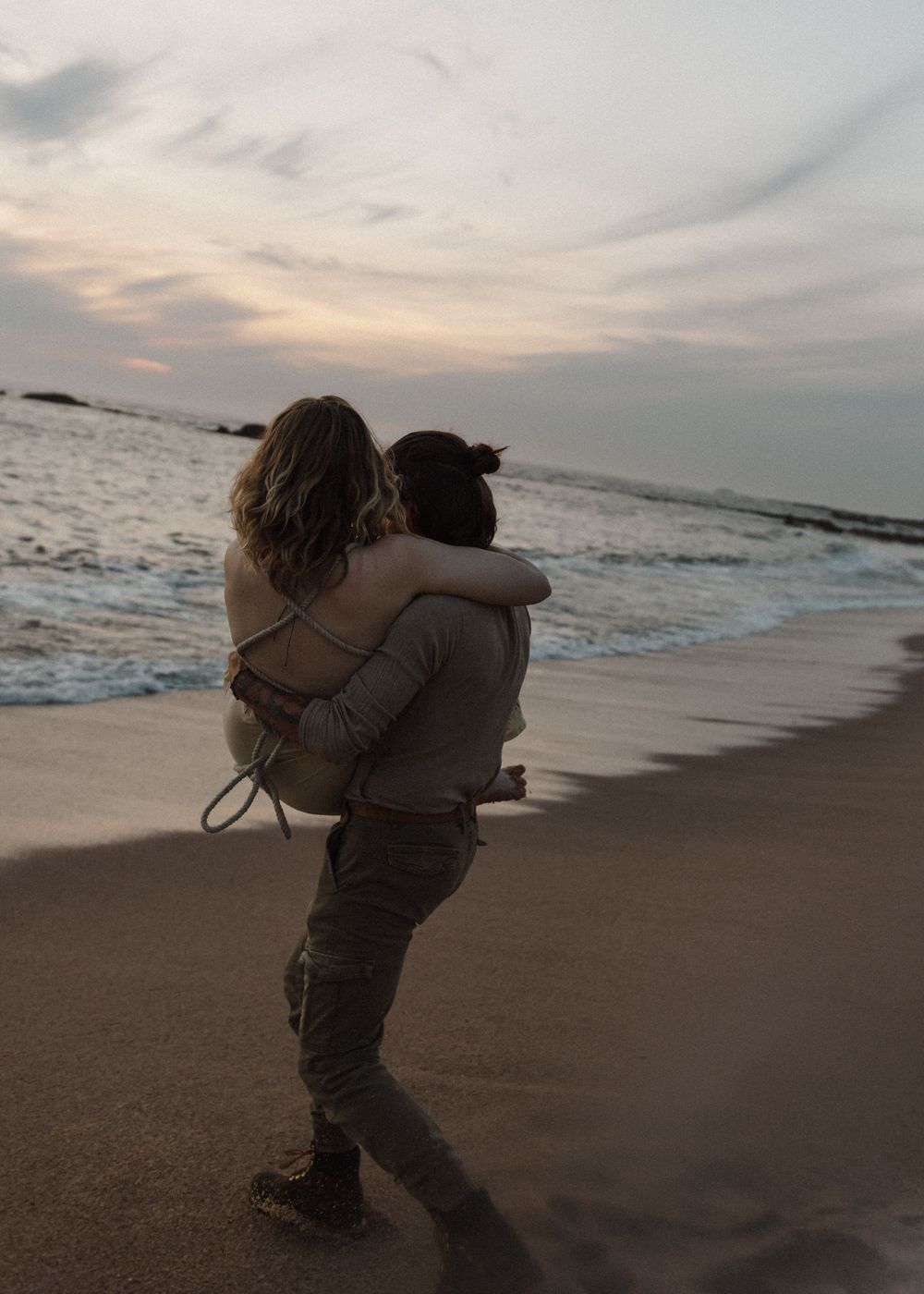 A couple embracing on a beach at sunset with waves crashing in the background.