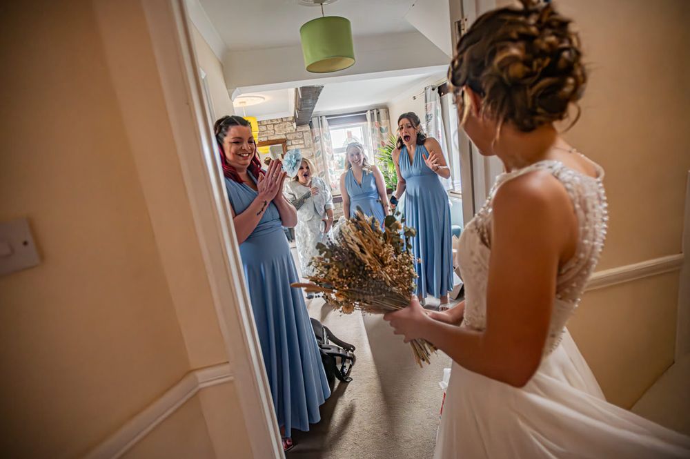 A bride shows off her dress for the first time to her bridesmaids and mother
