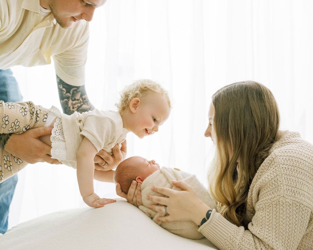 Family members sharing a tender moment together lying on white bedding in a sunlit room.