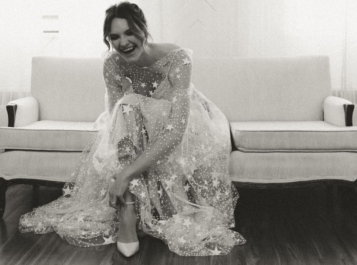 Black and white photo of bride in lace gown seated on sofa.