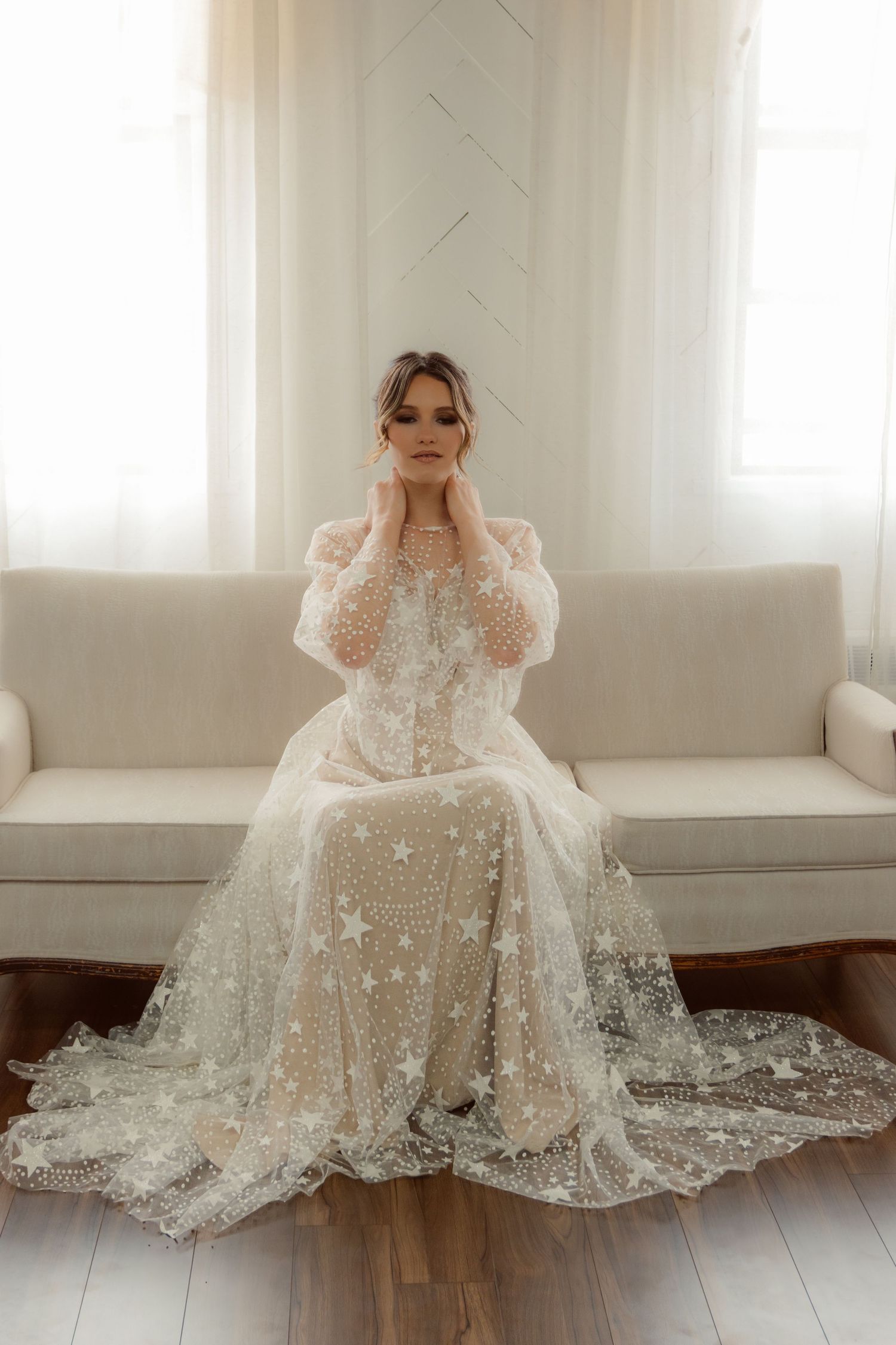 Bridal portrait featuring ethereal star-patterned wedding gown with sheer details on white couch.