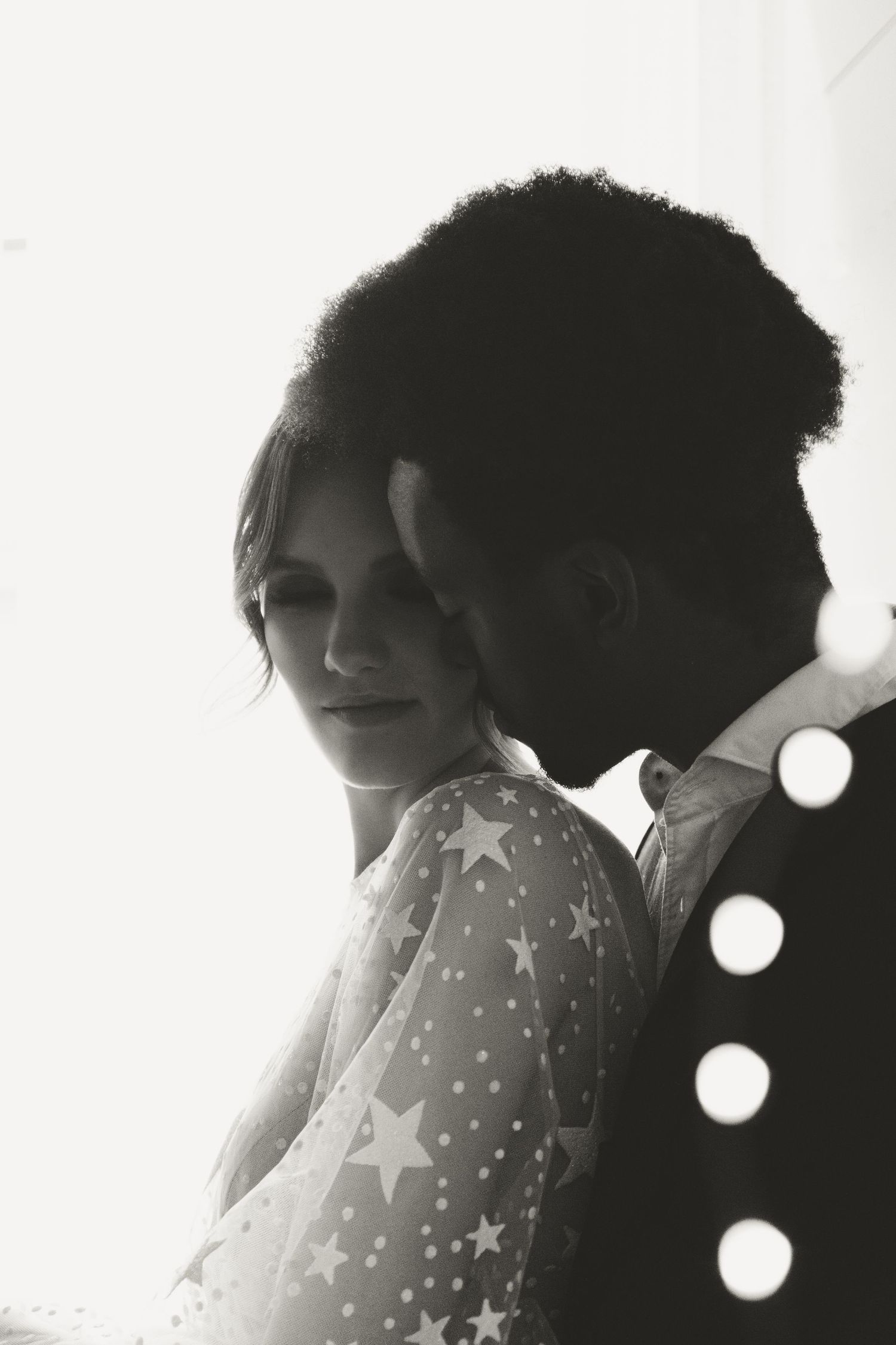 Artistic black and white photo showing romantic couple embracing, with star-patterned sheer dress details.