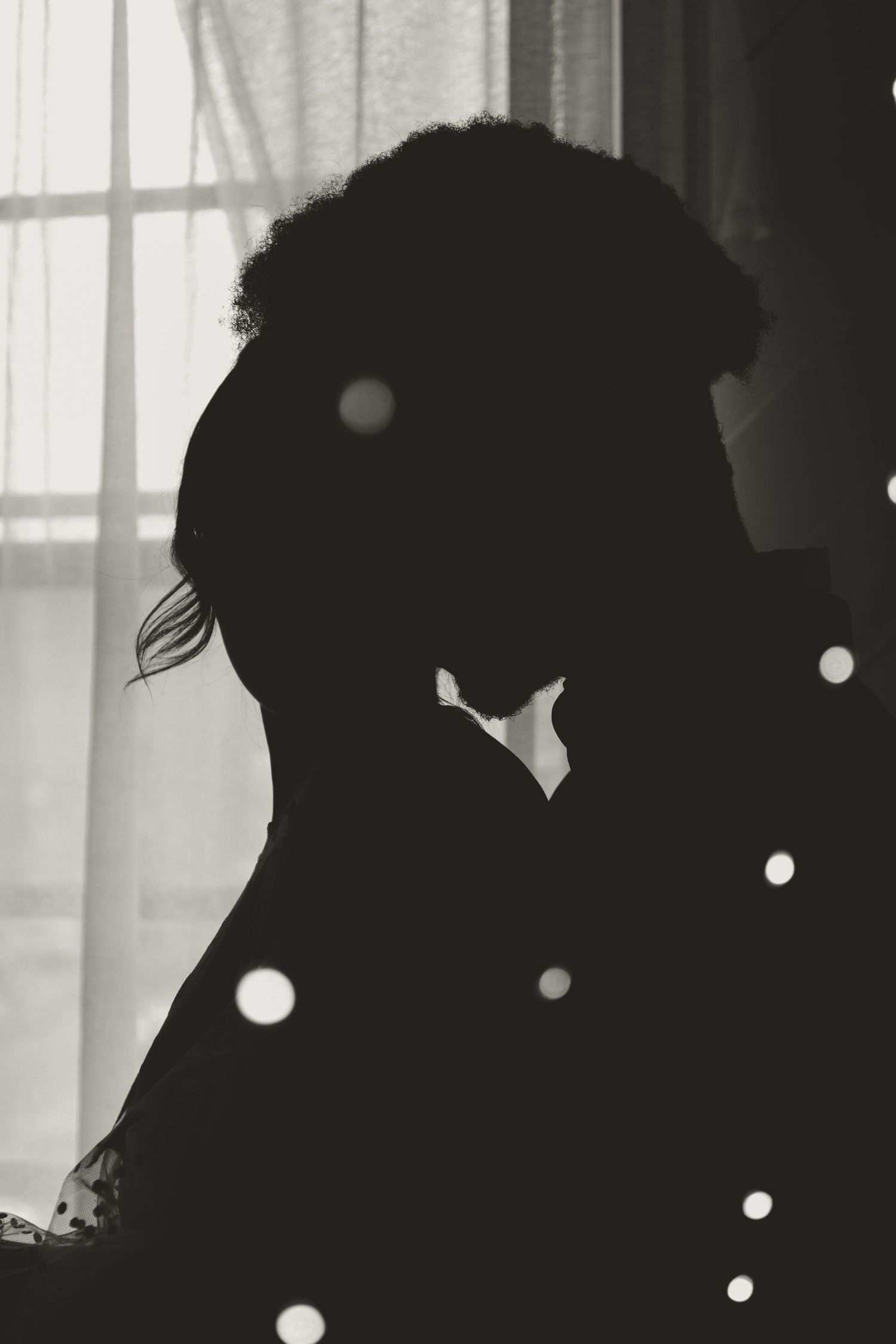 Silhouetted couple in romantic pose by window with bokeh light effects in black and white.