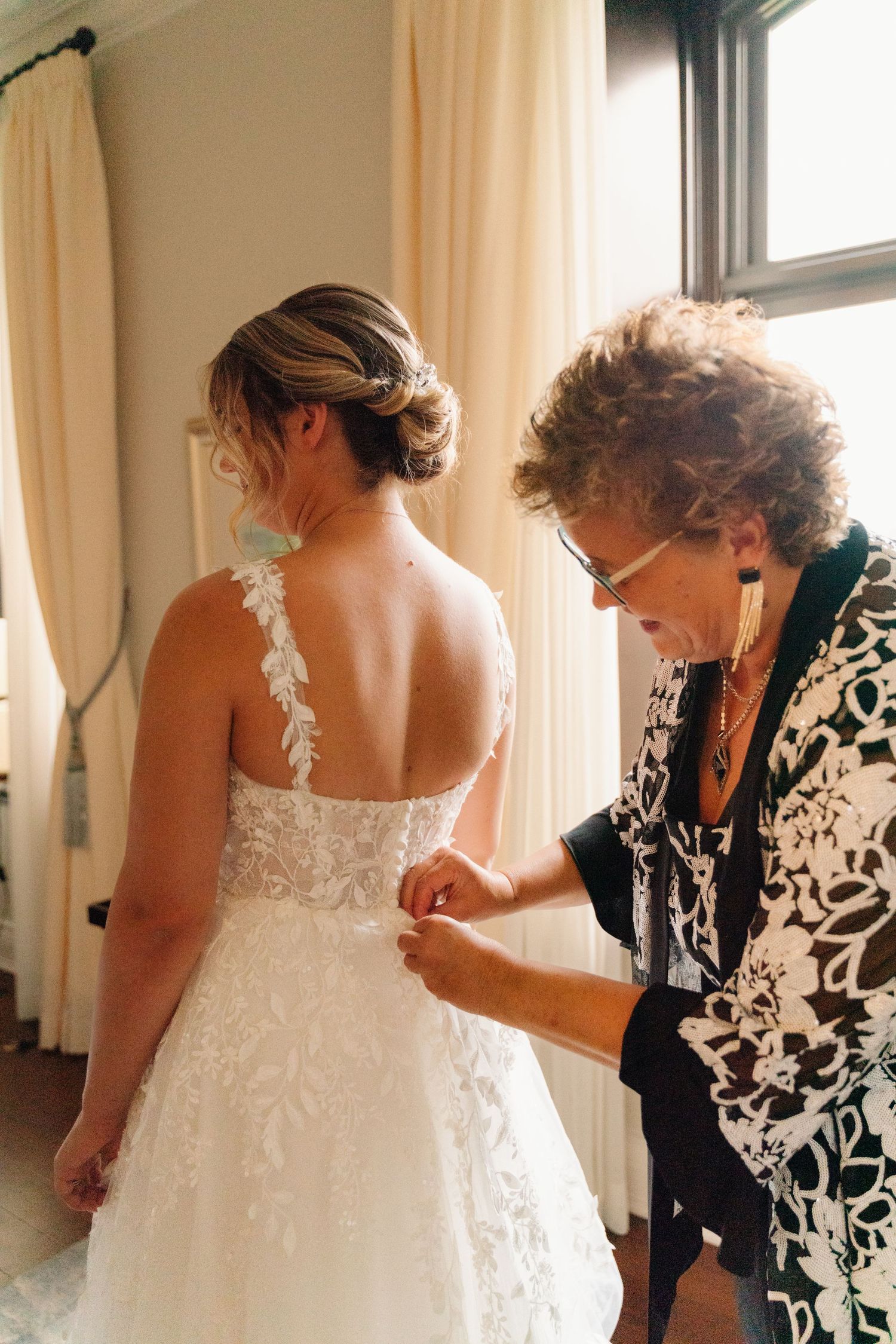 Back view of bride in lace wedding dress getting final adjustments before ceremony.