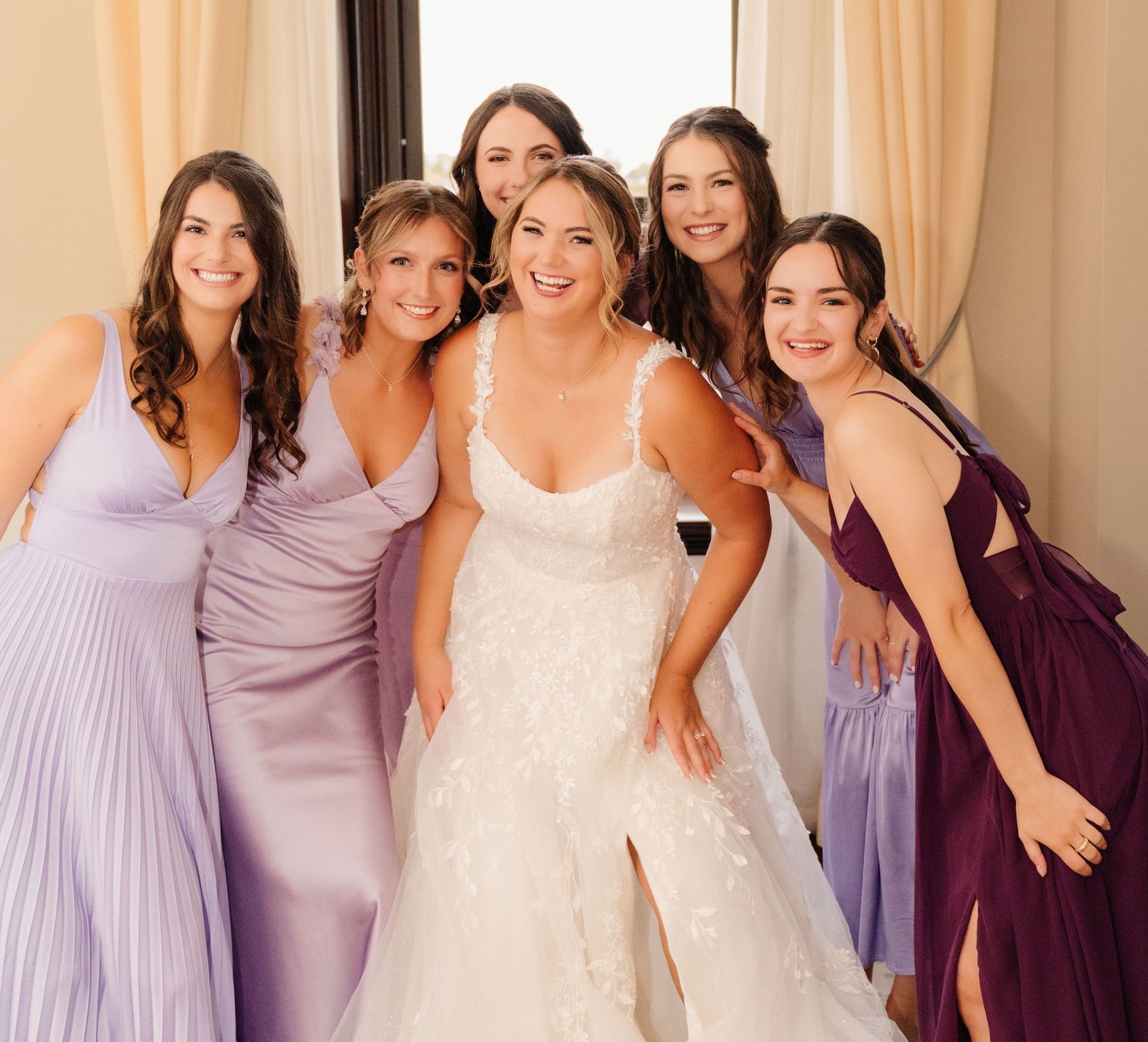 Bridal party in purple and lavender dresses posing together for formal photo.