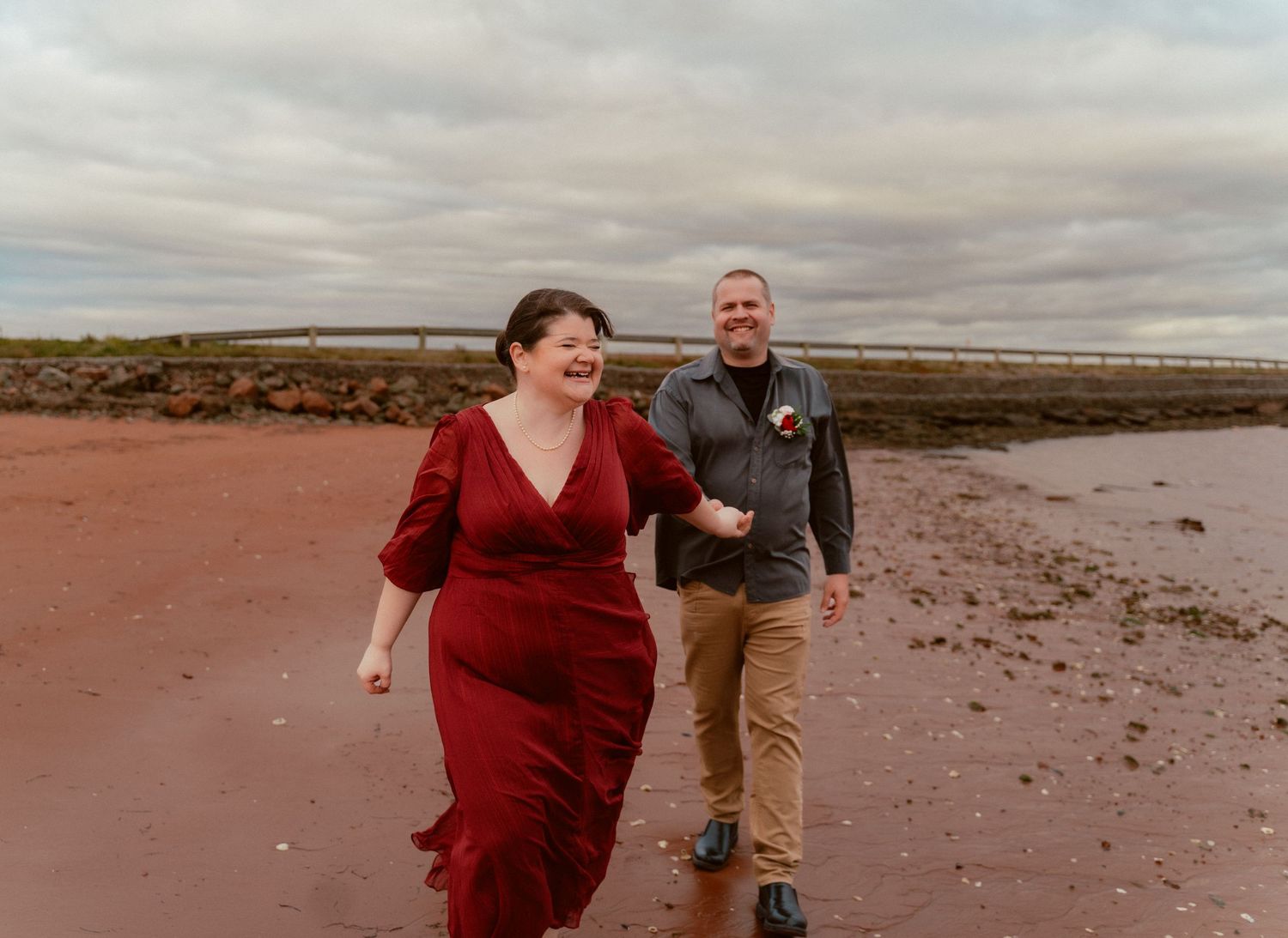 A couple shares a happy moment while walking on a red sand beach.