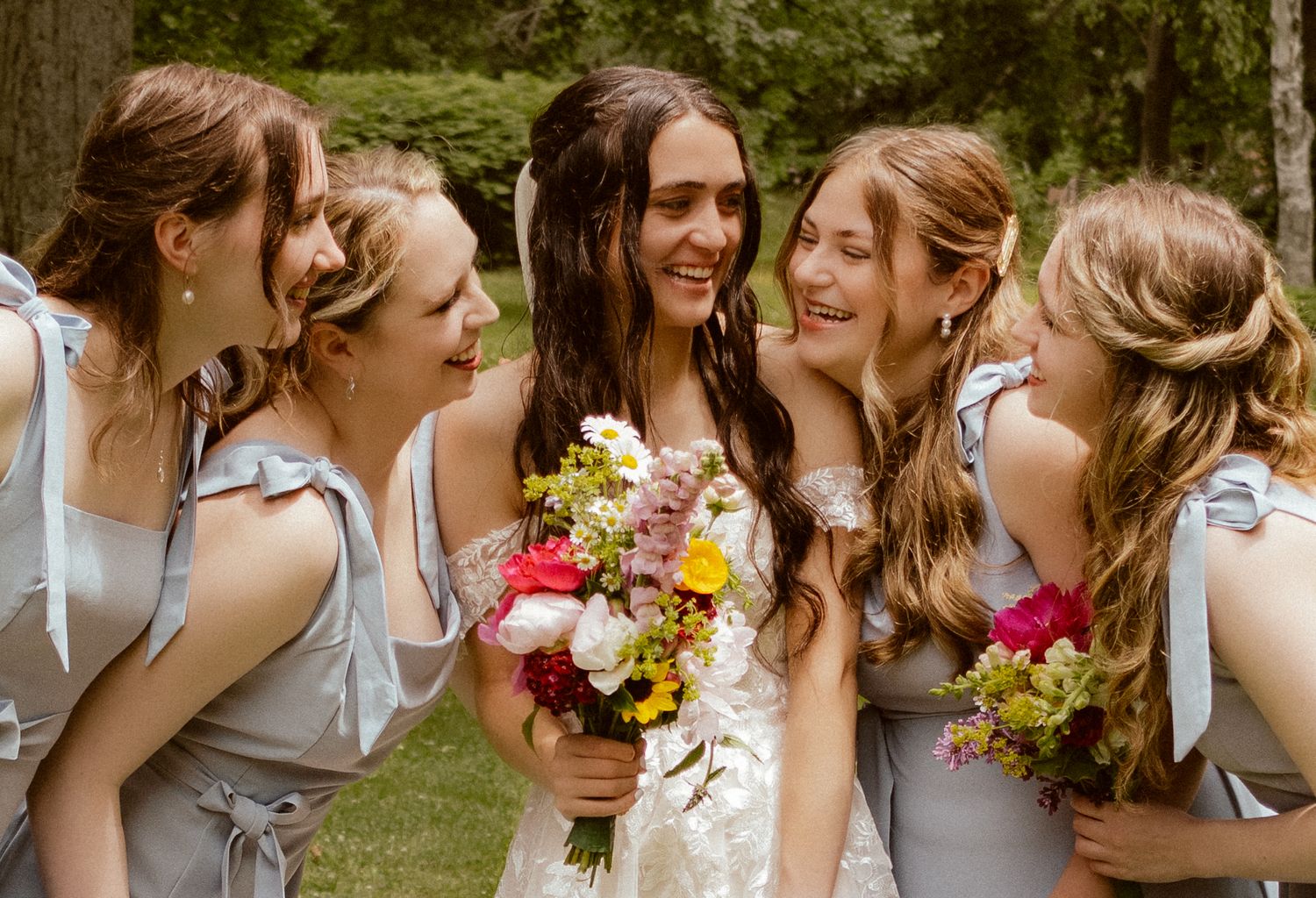 Bride and bridesmaids sharing laughter while holding colorful floral bouquets.