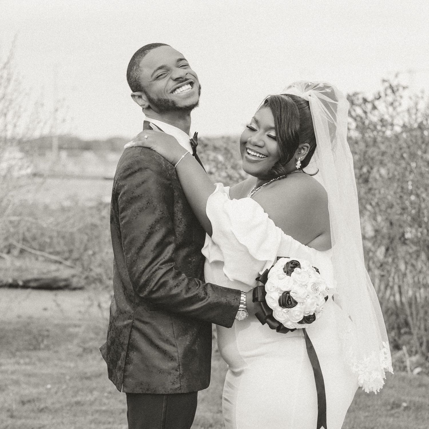A happy couple laughing together on their wedding day with the bride holding a soccer ball bouquet.
