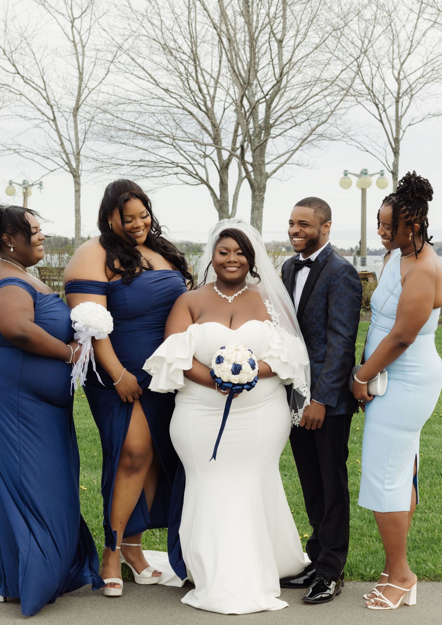 A wedding party in navy blue and white dresses poses together on a cloudy day outdoors.