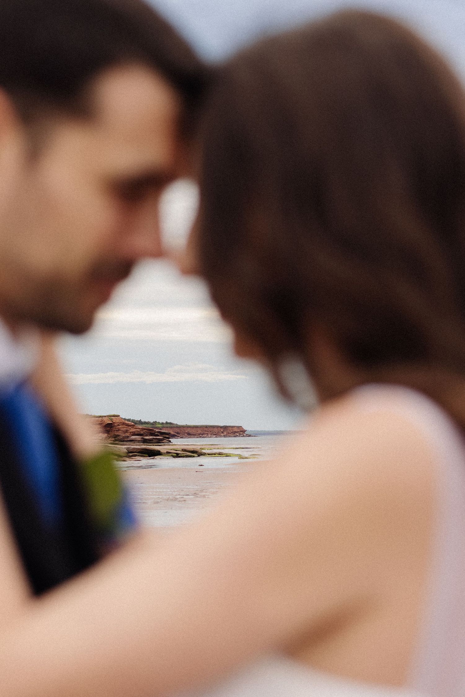 A romantic moment captured at a coastal beach with rocky shoreline in the background.