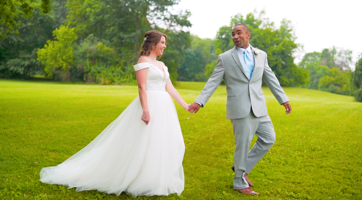 Wedding couple dances joyfully in an outdoor garden setting with lush greenery and natural lighting.