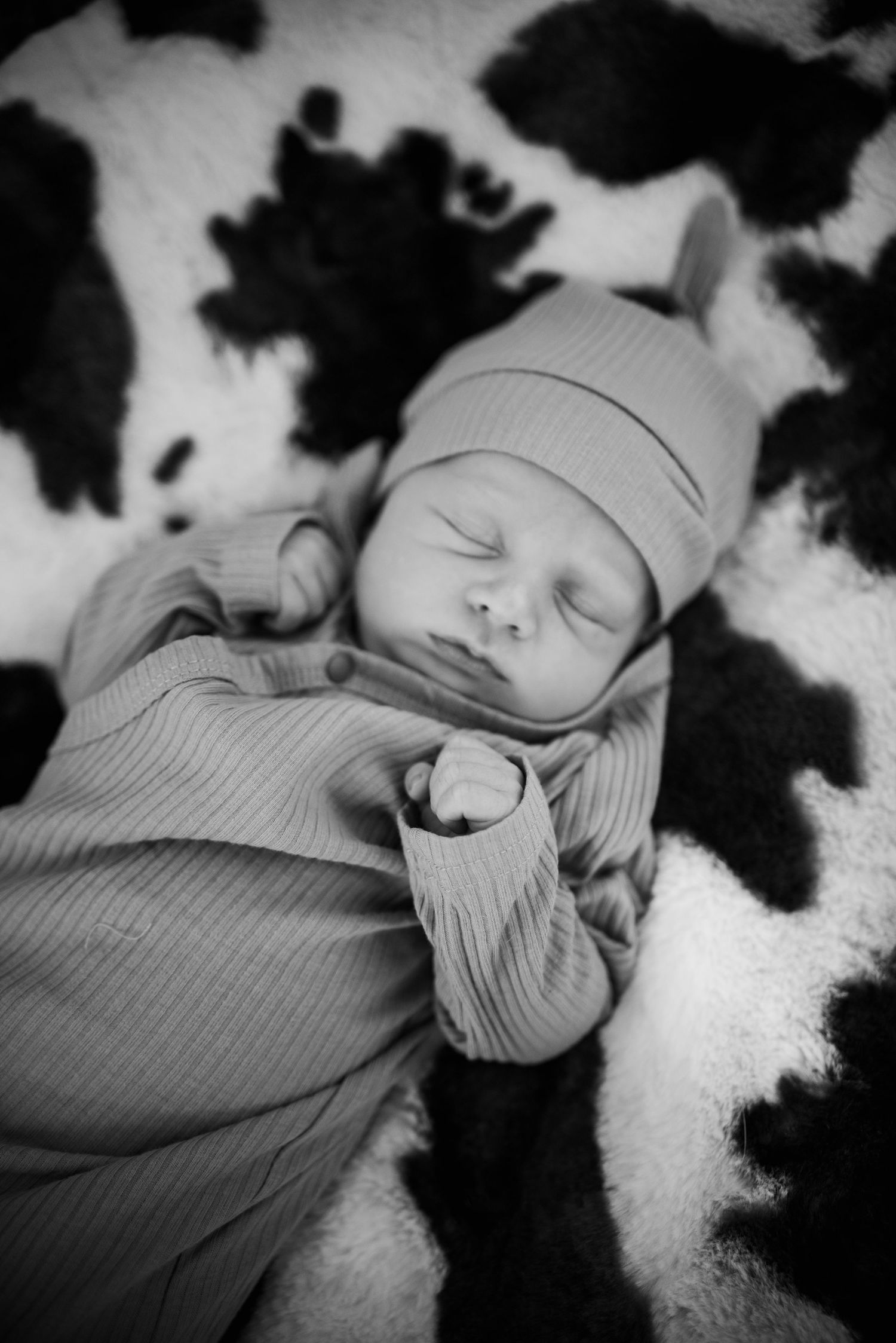 Sleeping newborn wrapped in soft ribbed fabric on textured black and white background.