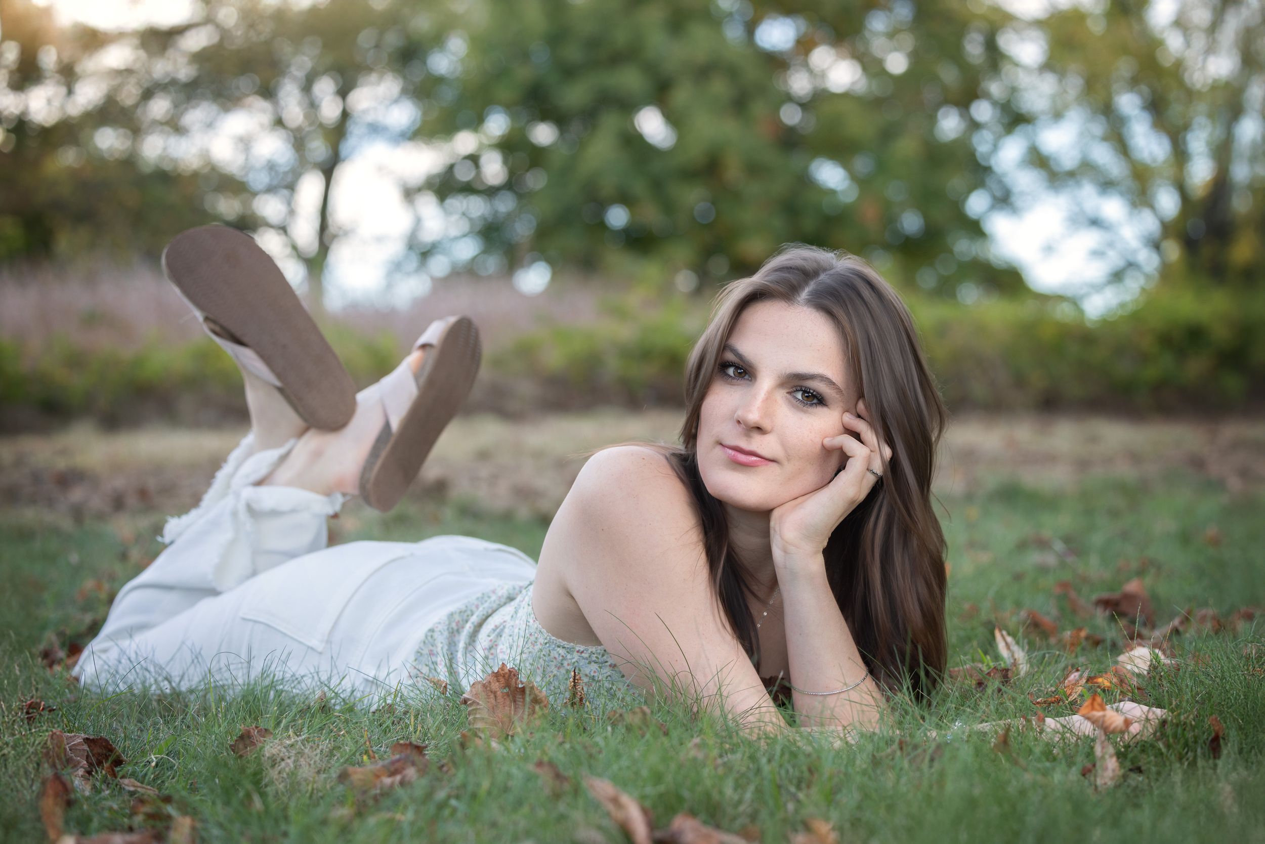 A person in a white lying on autumn leaves in an outdoor setting makes graceful poses.