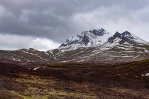 Rugged mountain peak covered in snow under stormy skies in a desolate highland landscape.