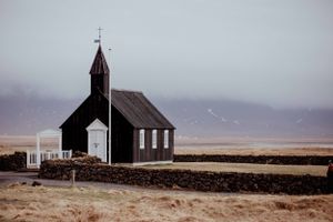 Solitary black wooden church stands in a barren landscape under overcast skies.