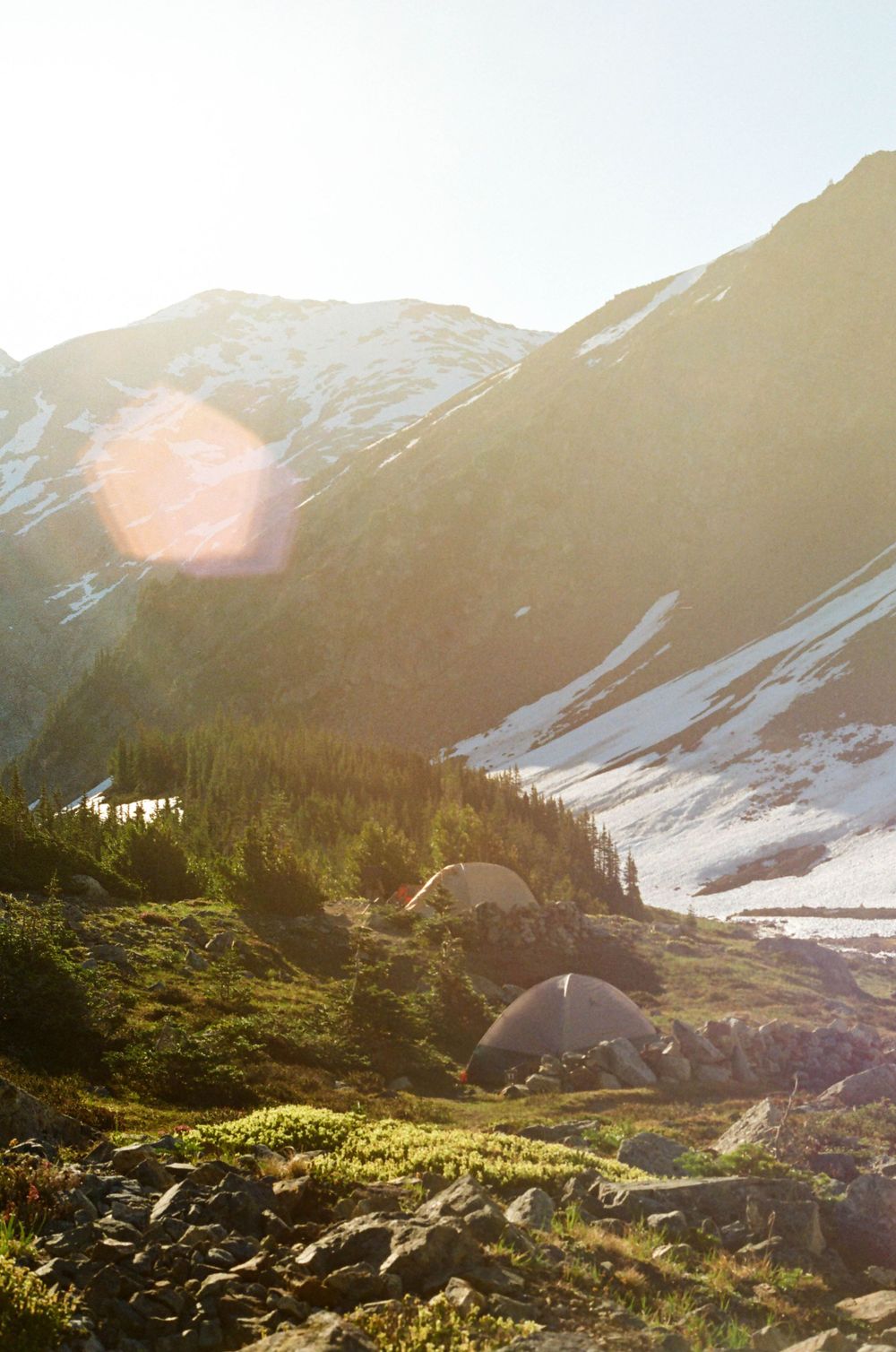 Mountain camping scene at sunset with tents pitched among alpine wilderness.