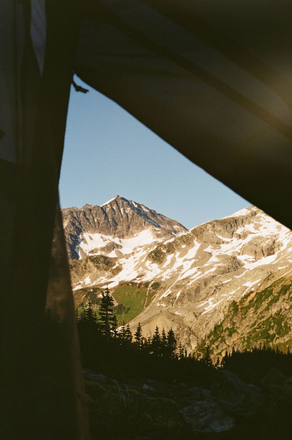 Snow-capped mountain peaks viewed through a natural frame in dramatic lighting.