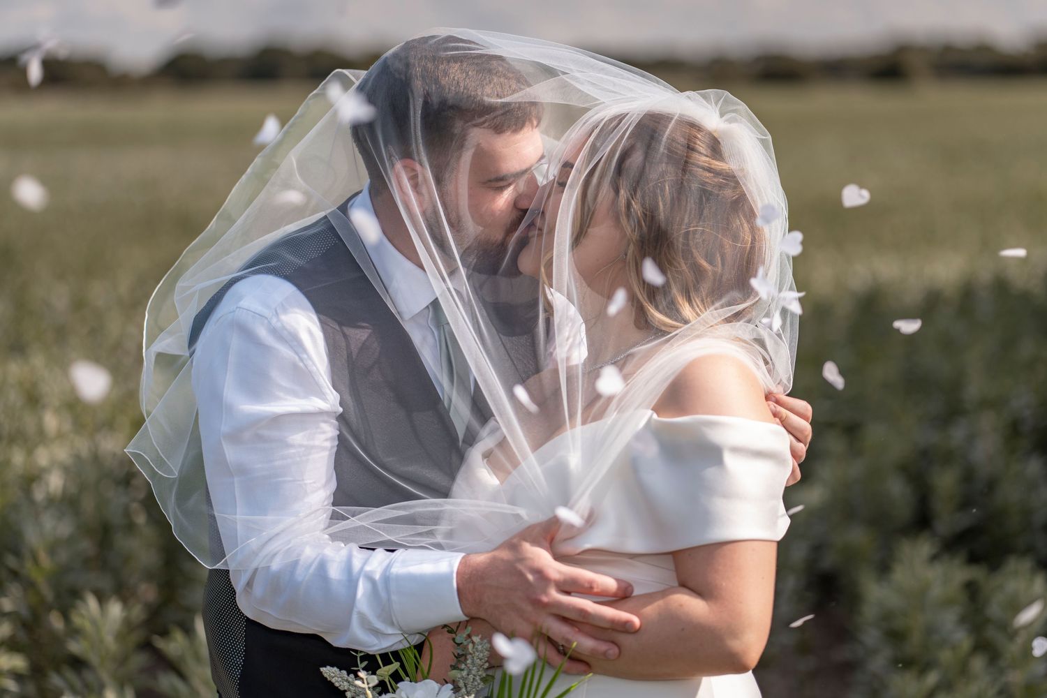 Romantic wedding couple embracing in a sunlit outdoor setting with flowing veil.