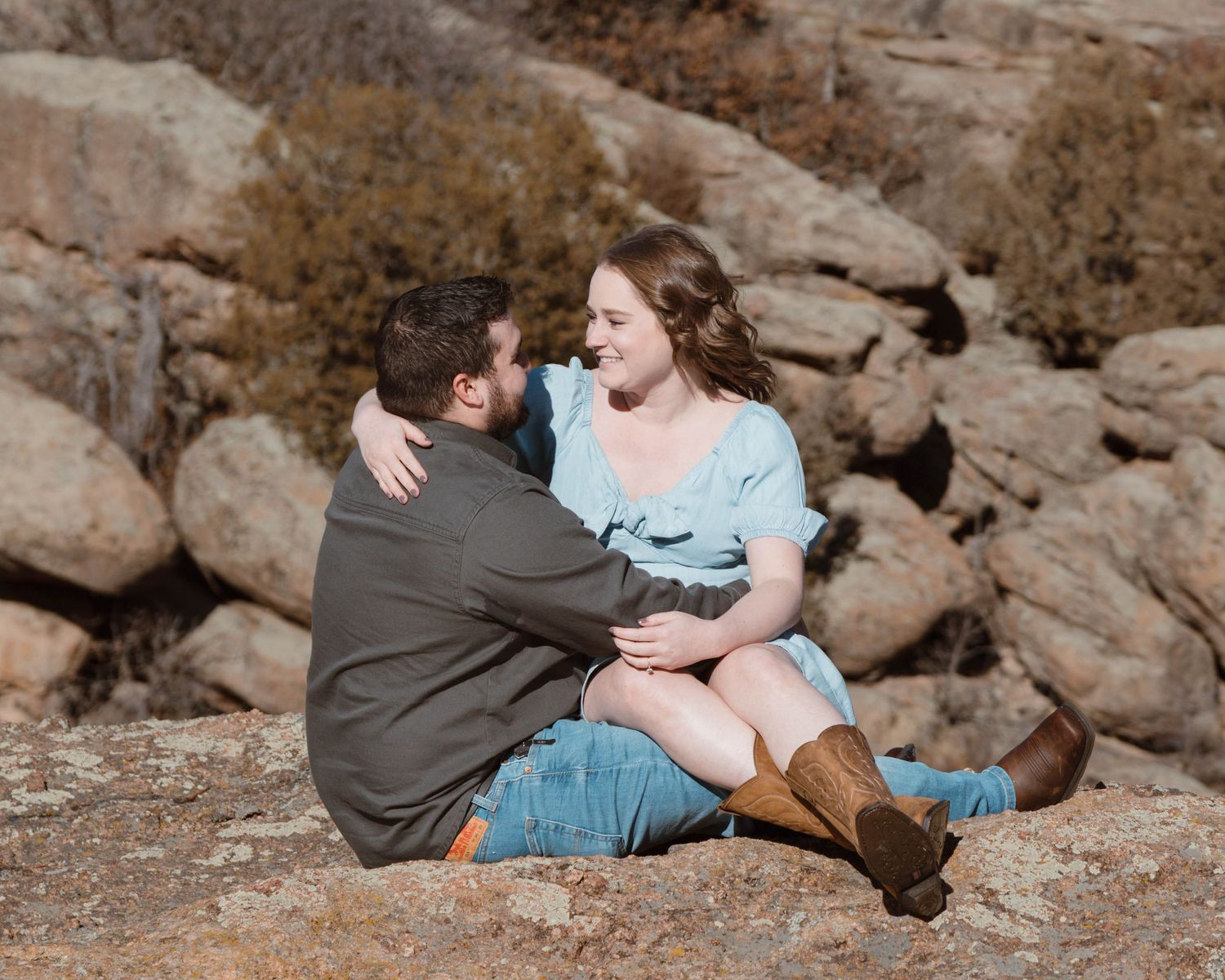 A couple embraces while sitting among rocky terrain during an engagement photoshoot.