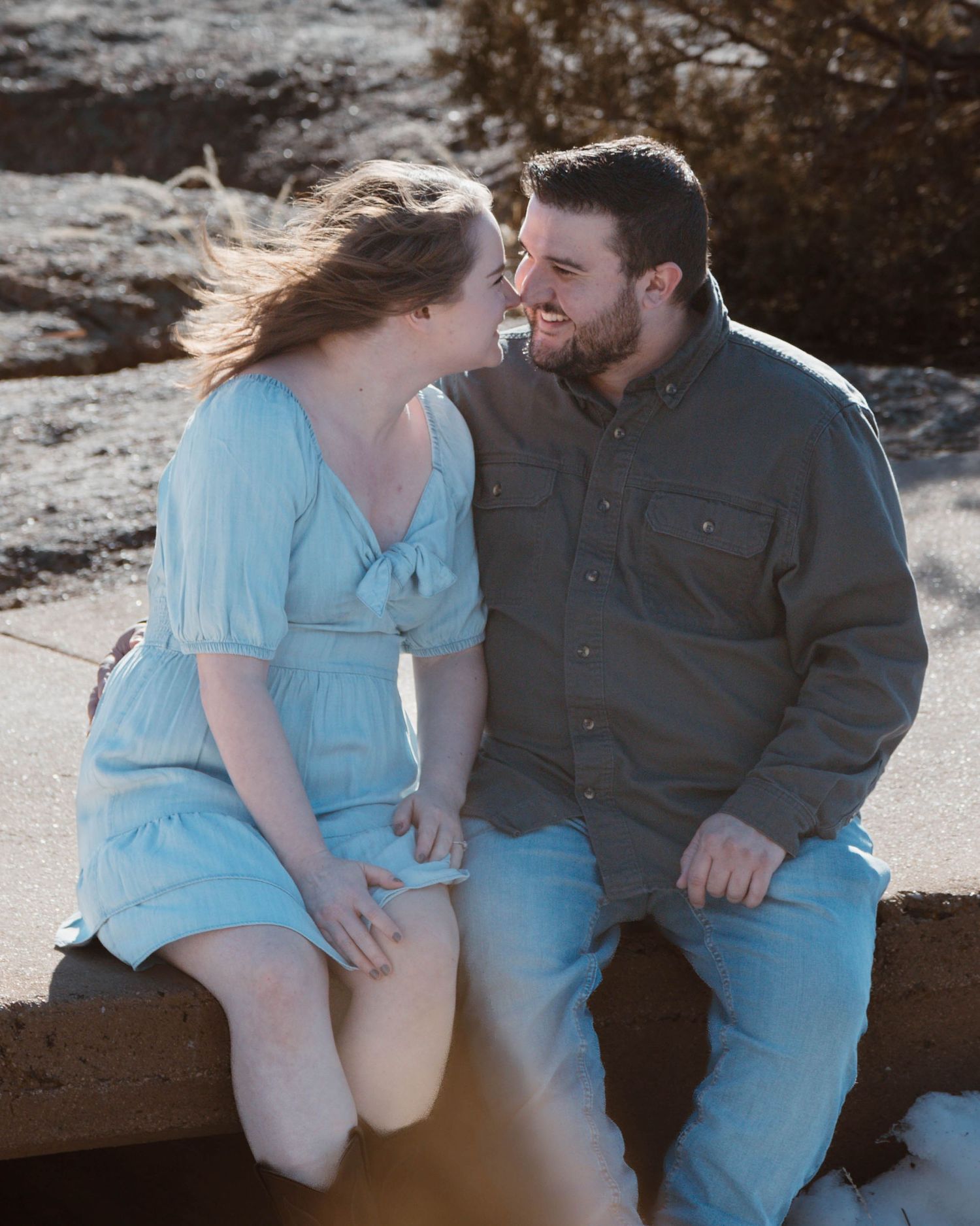 A couple shares an intimate moment while sitting on rocks during sunset.