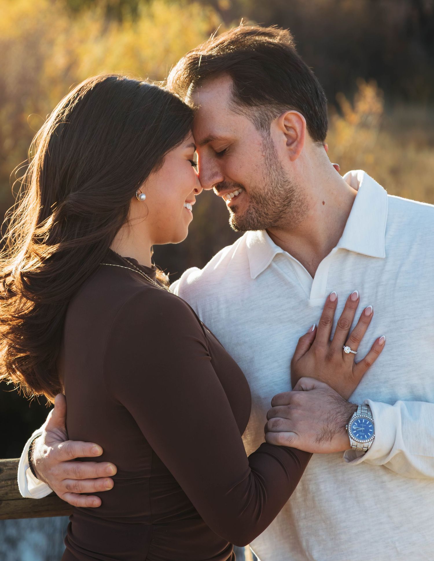 A romantic couple embraces in soft golden sunlight during an outdoor photoshoot.