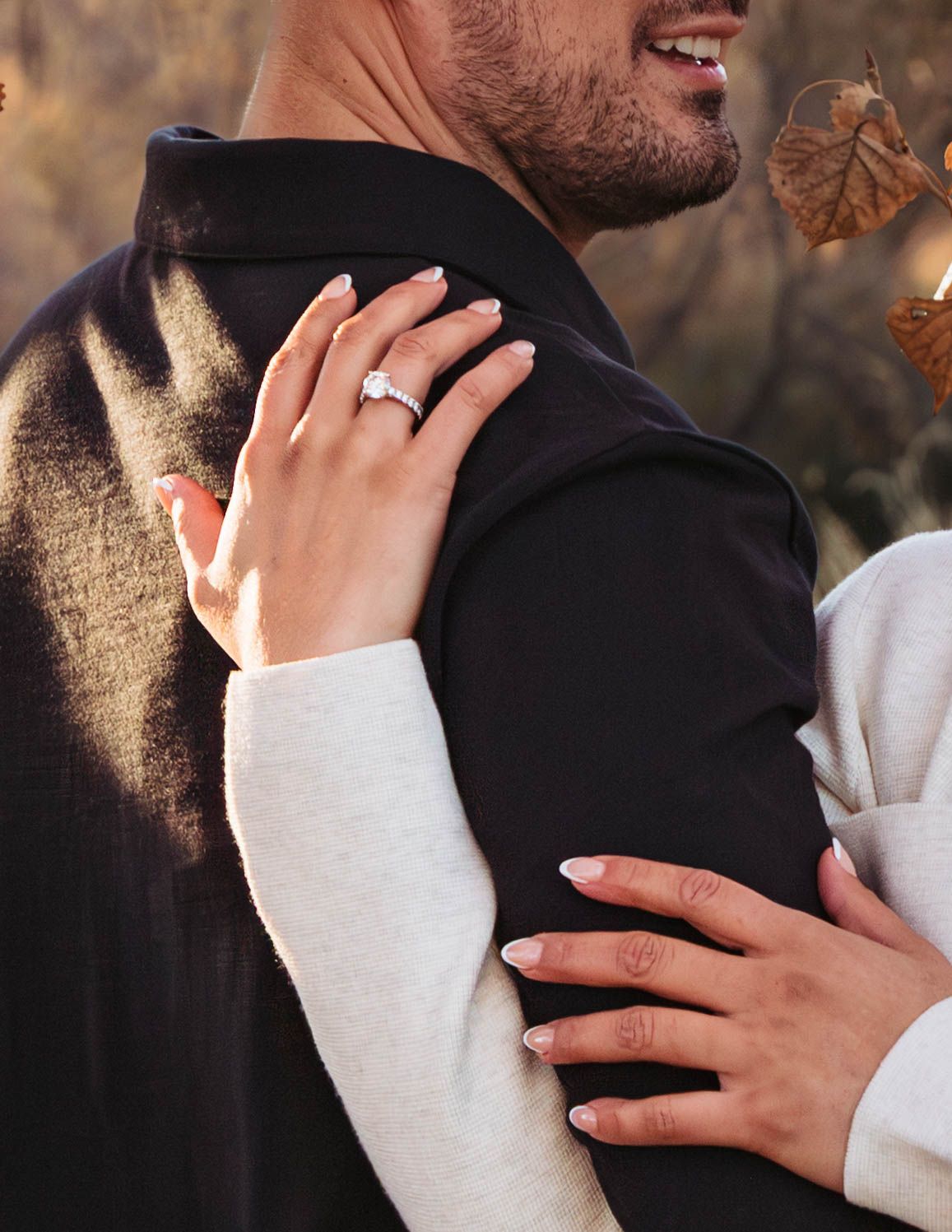Close-up of hands wearing engagement ring embracing in romantic outdoor autumn setting.