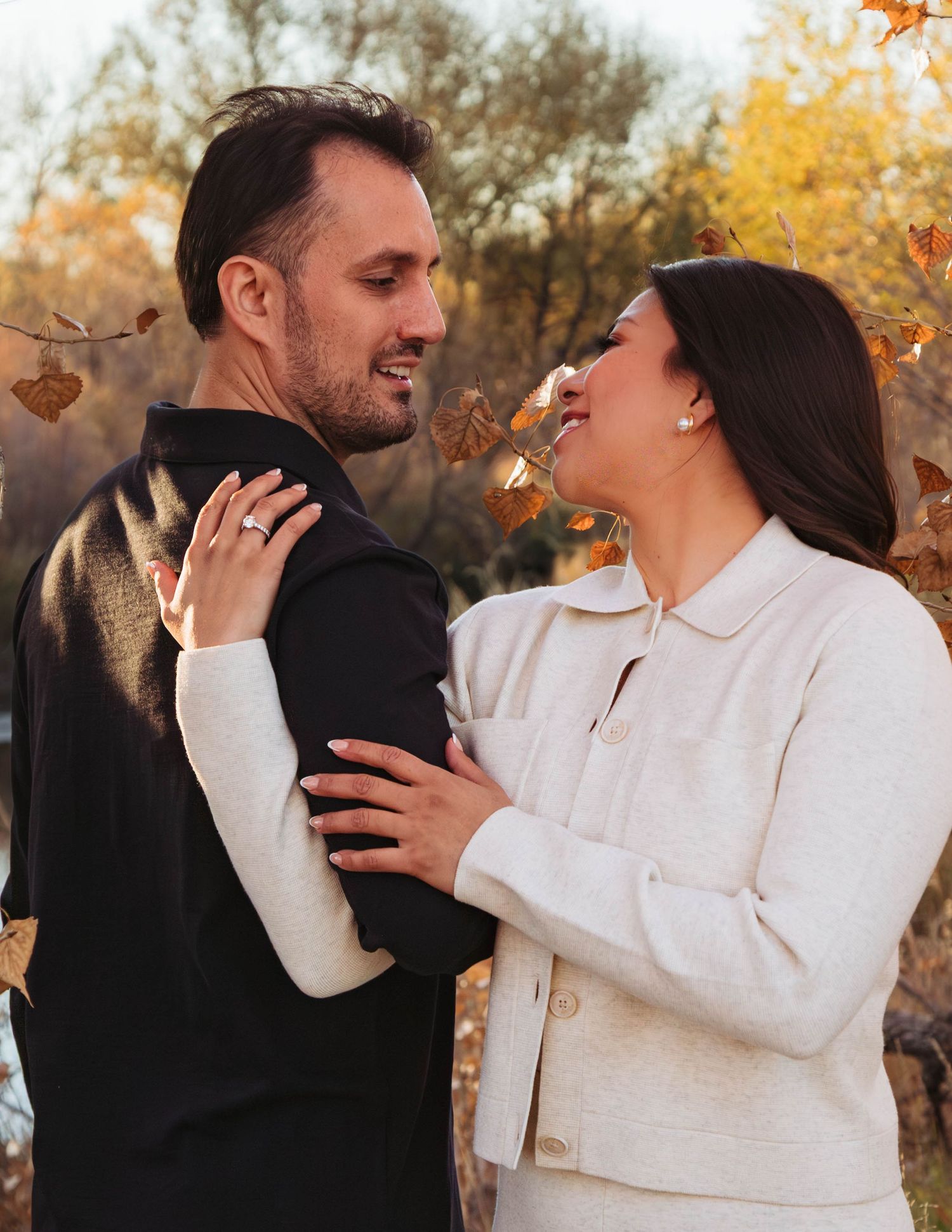 A couple embraces and laughs together during a fall photoshoot with golden autumn leaves in the background.