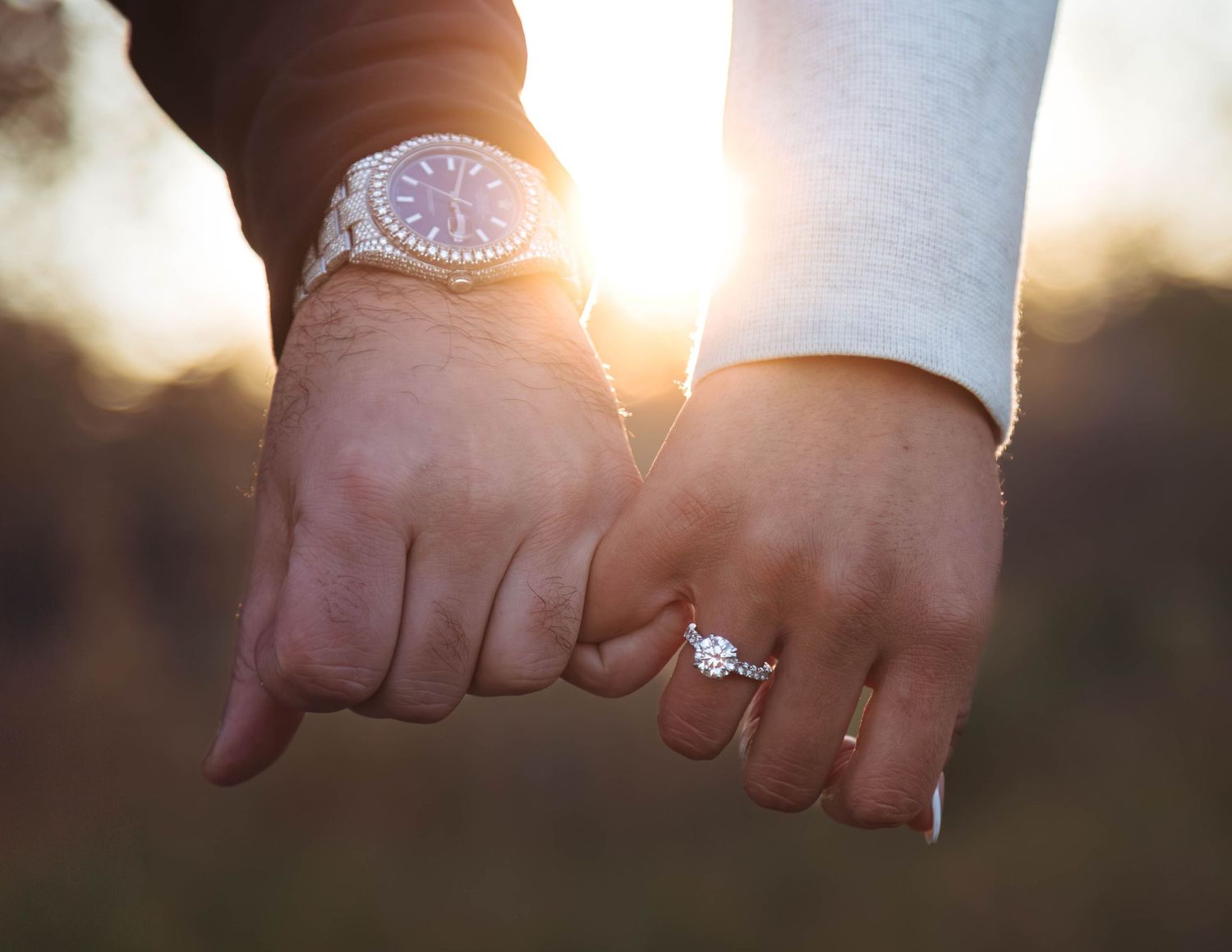 Close-up of engaged couple's hands showing off diamond engagement ring during golden sunset.