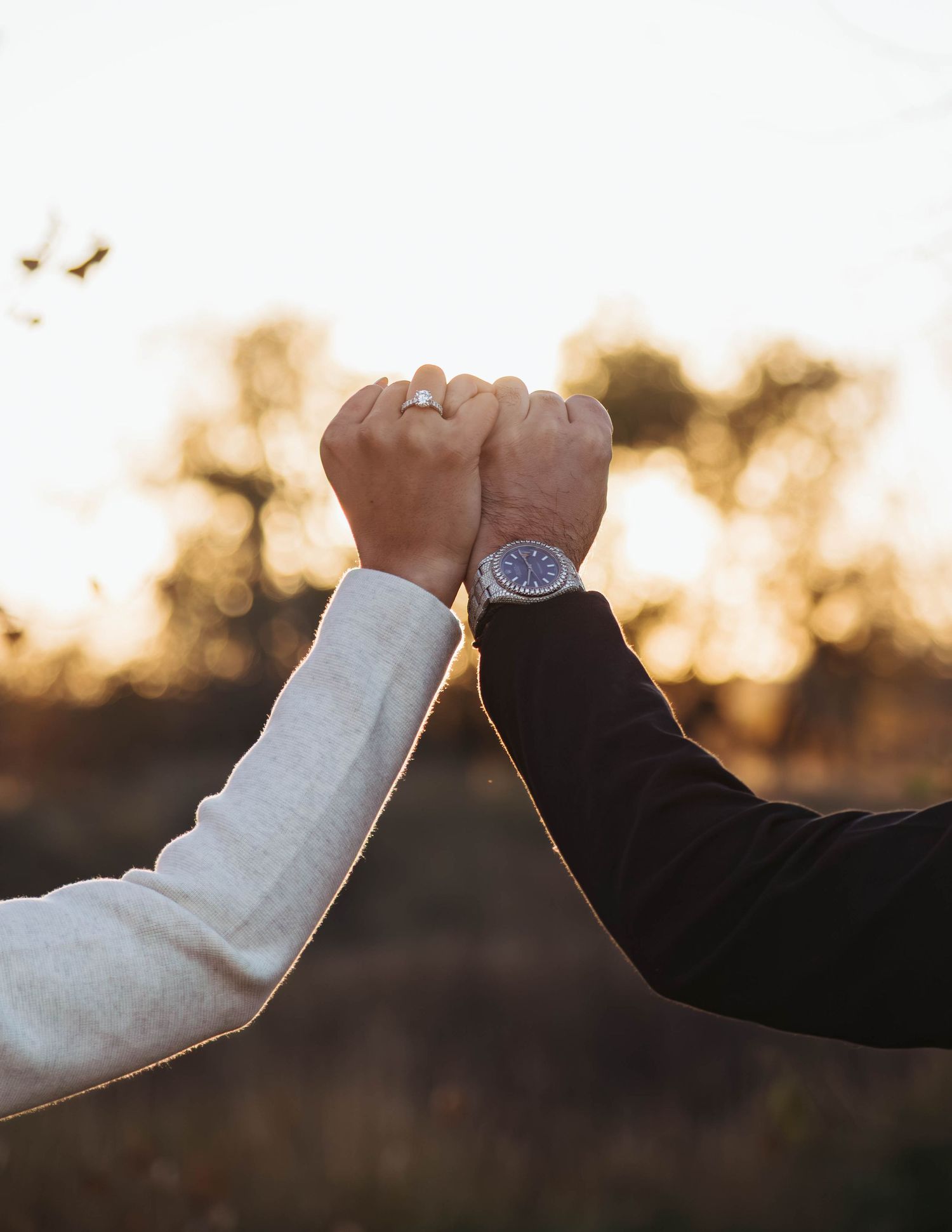 Two hands reach out to touch each other against a warm sunset sky in an intimate moment.
