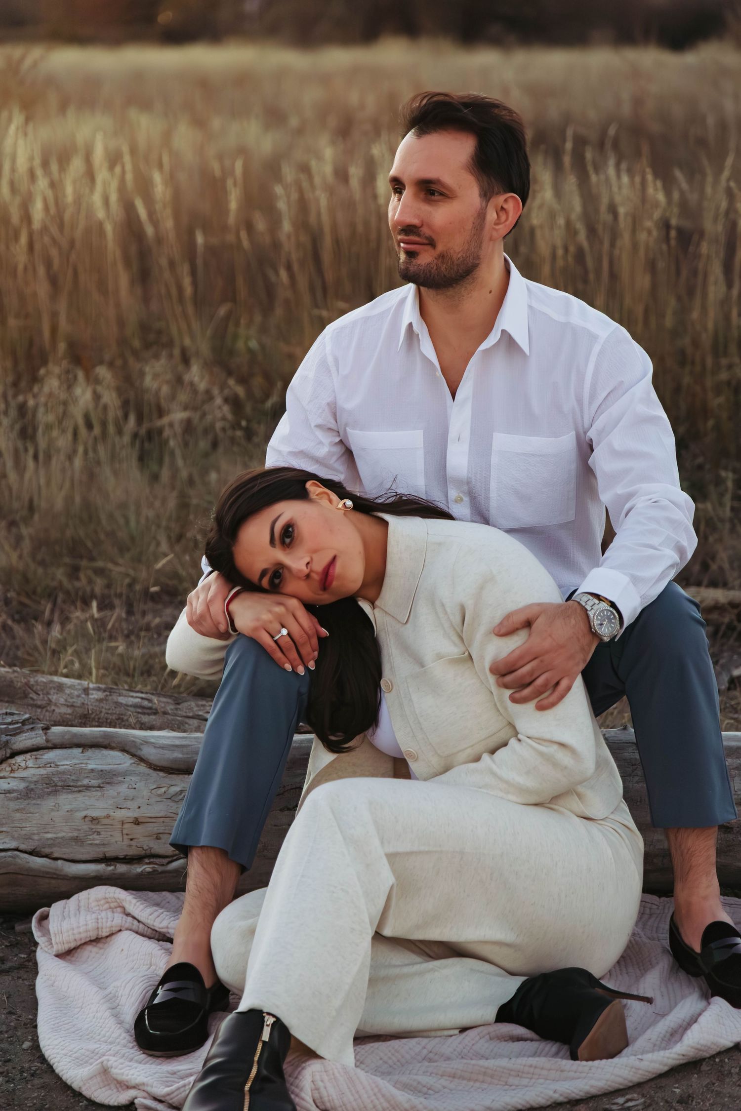 A couple sits together on a blanket in a rustic outdoor setting during golden hour.