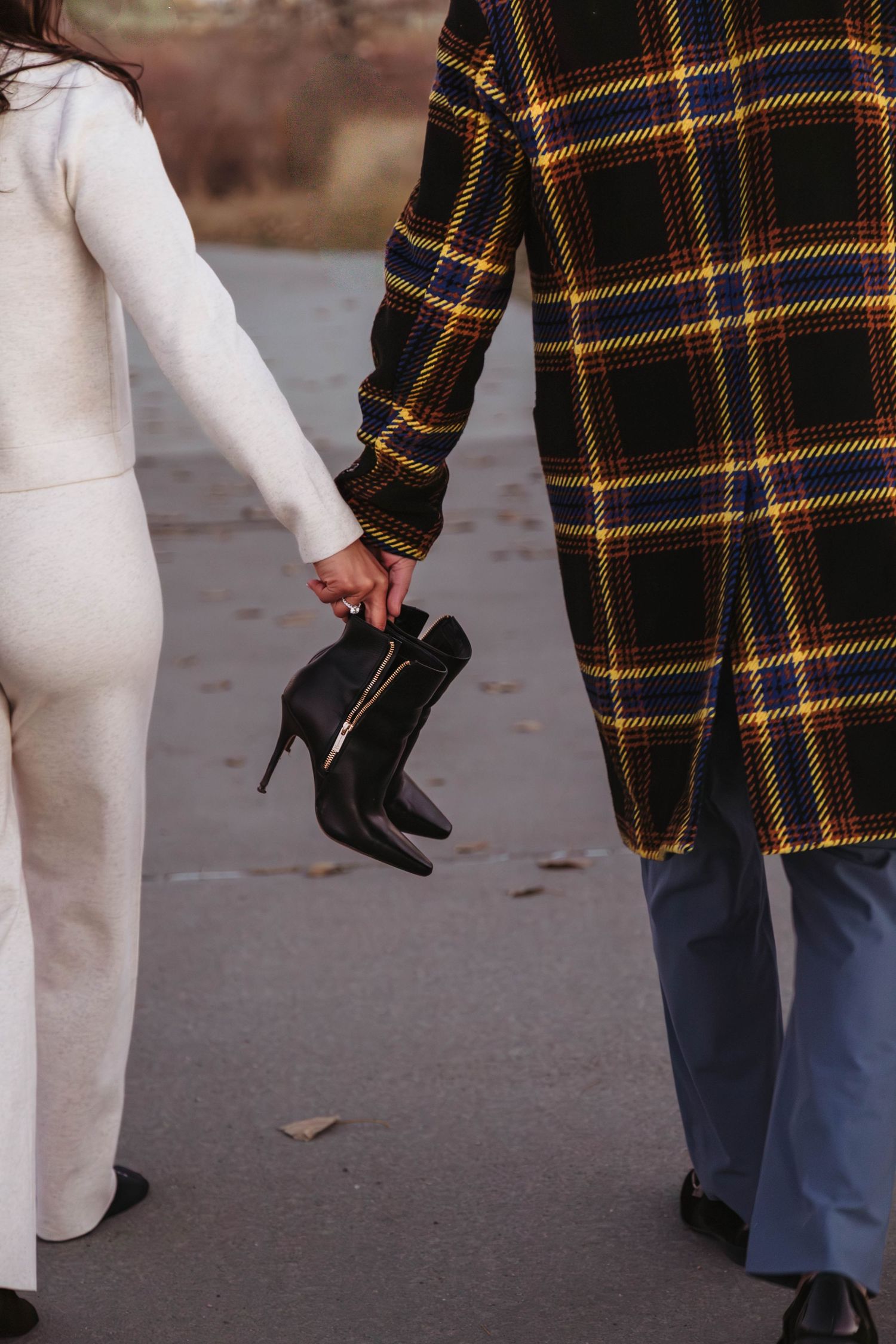 Fashion detail shot showing plaid coat and white dress with black boots against autumn leaves on ground.