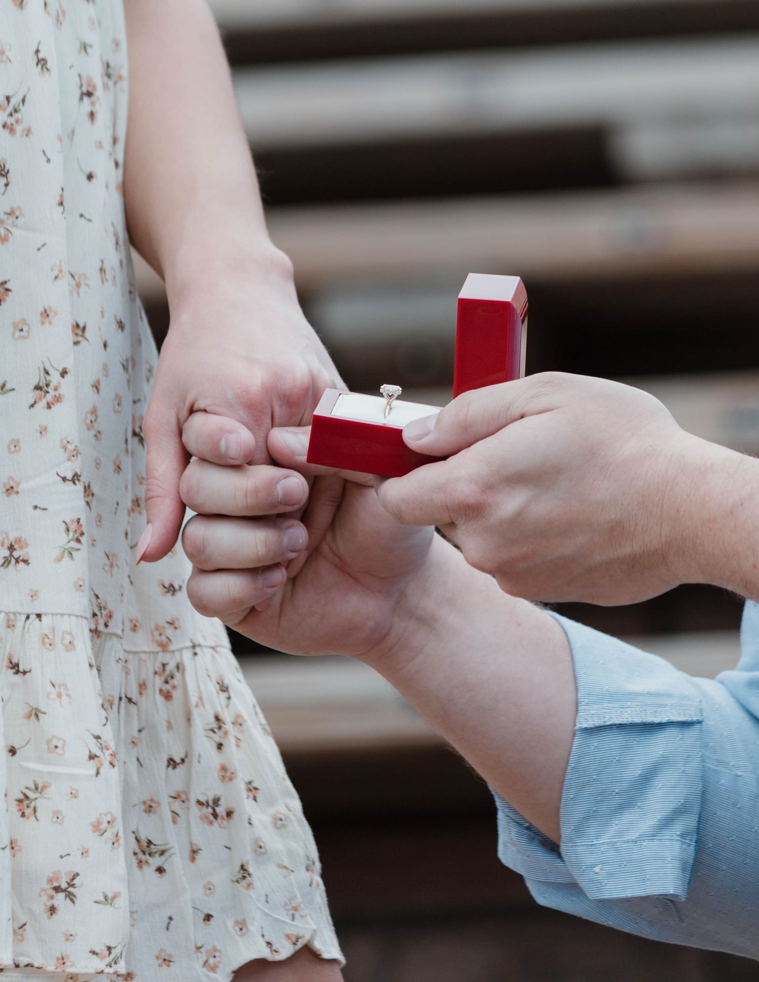 Close-up of hands presenting an engagement ring in a red box during a proposal moment.
