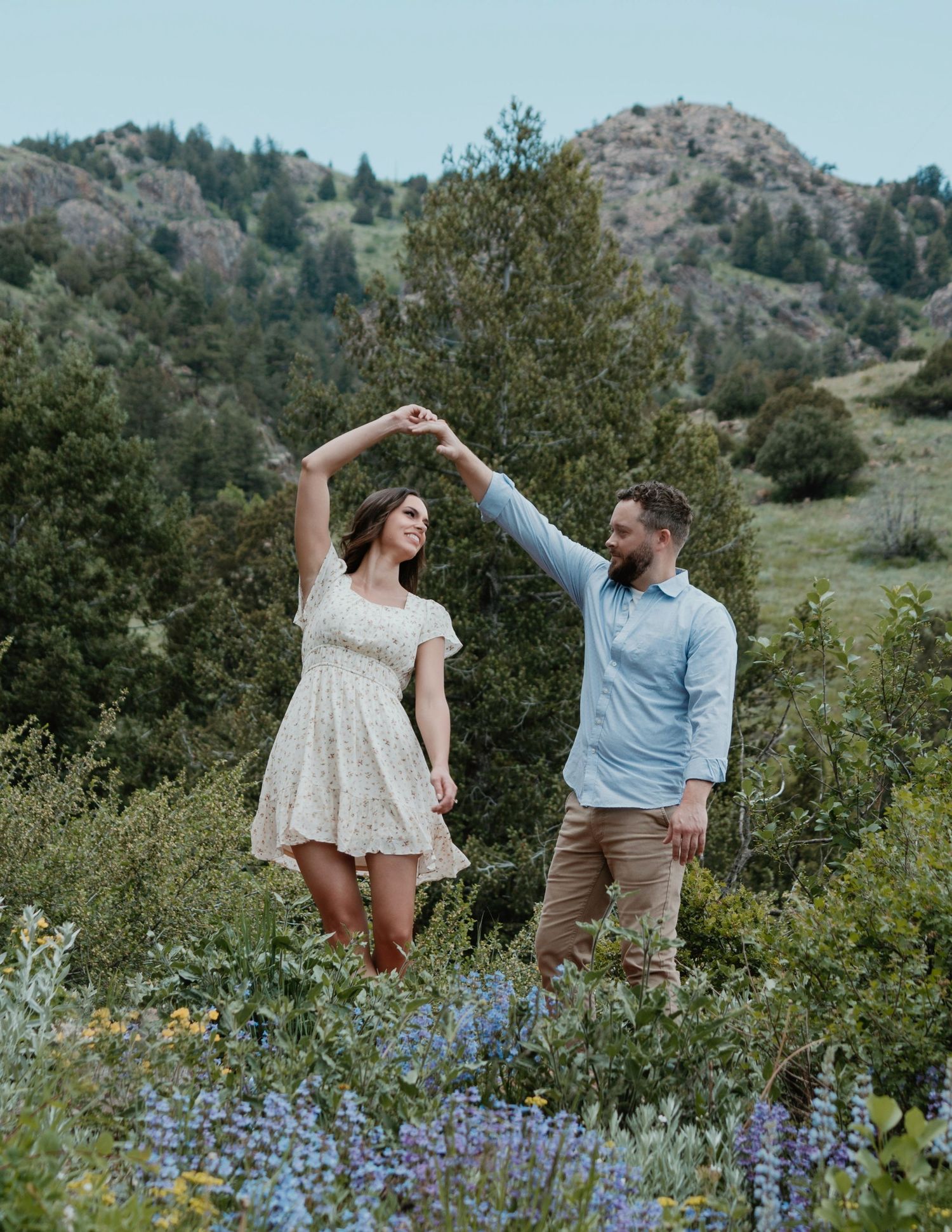 A couple dances together among purple wildflowers with mountains in the background.
