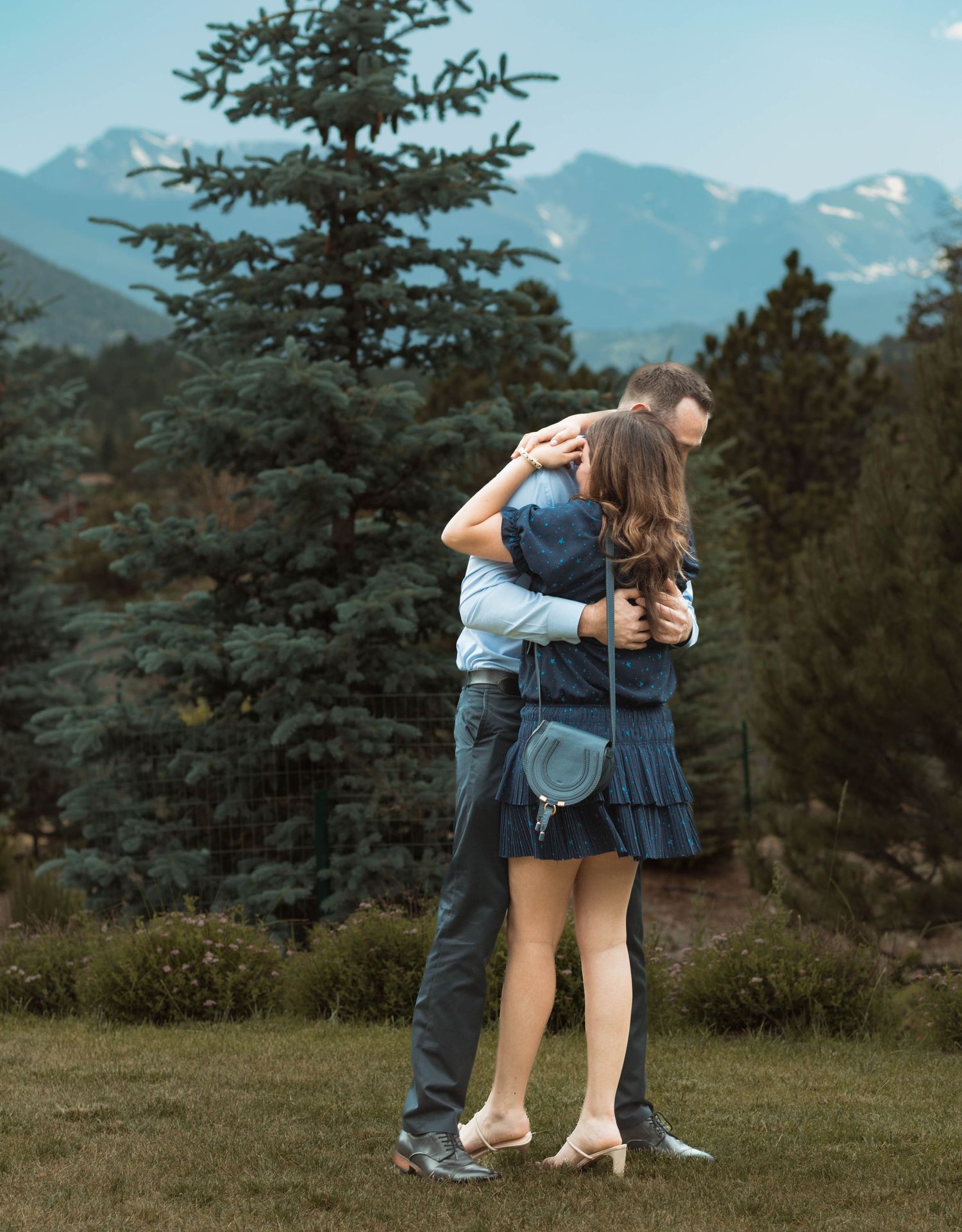 A joyful embrace after a proposal with snow-capped mountains and evergreen trees in the background.