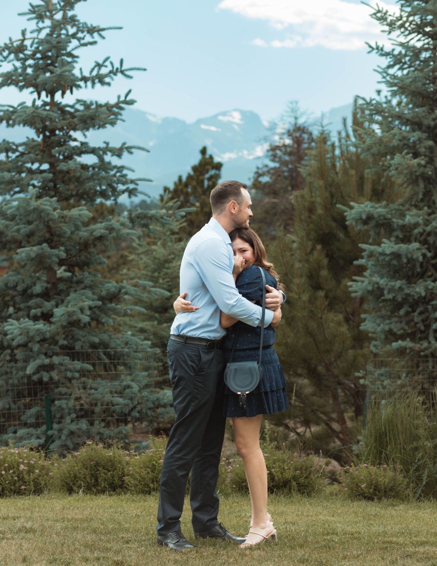A romantic embrace against a backdrop of mountains and evergreen trees.
