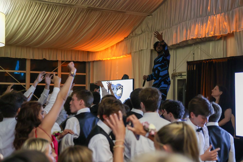 Energetic crowd with raised hands dancing at a party under draped tent ceiling.